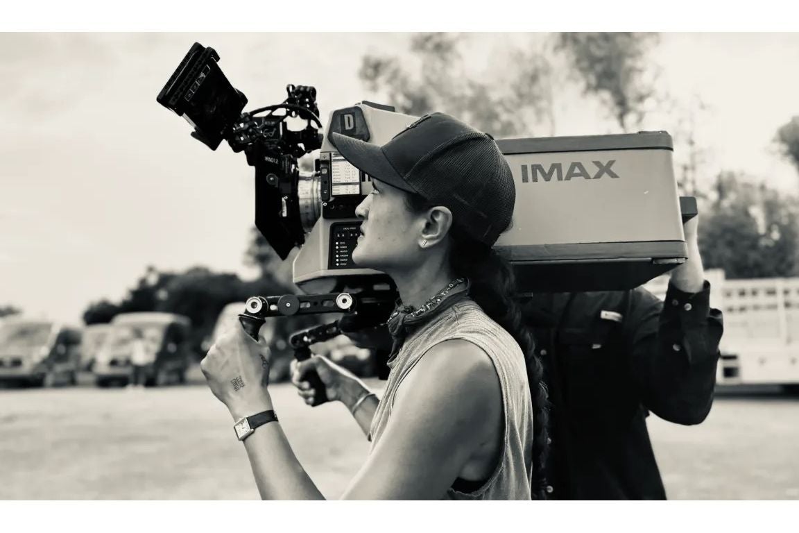 A woman in a tank top holds a large film camera