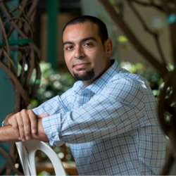 A man in a checked shirt sits in a relaxed position on a chair turned backwards