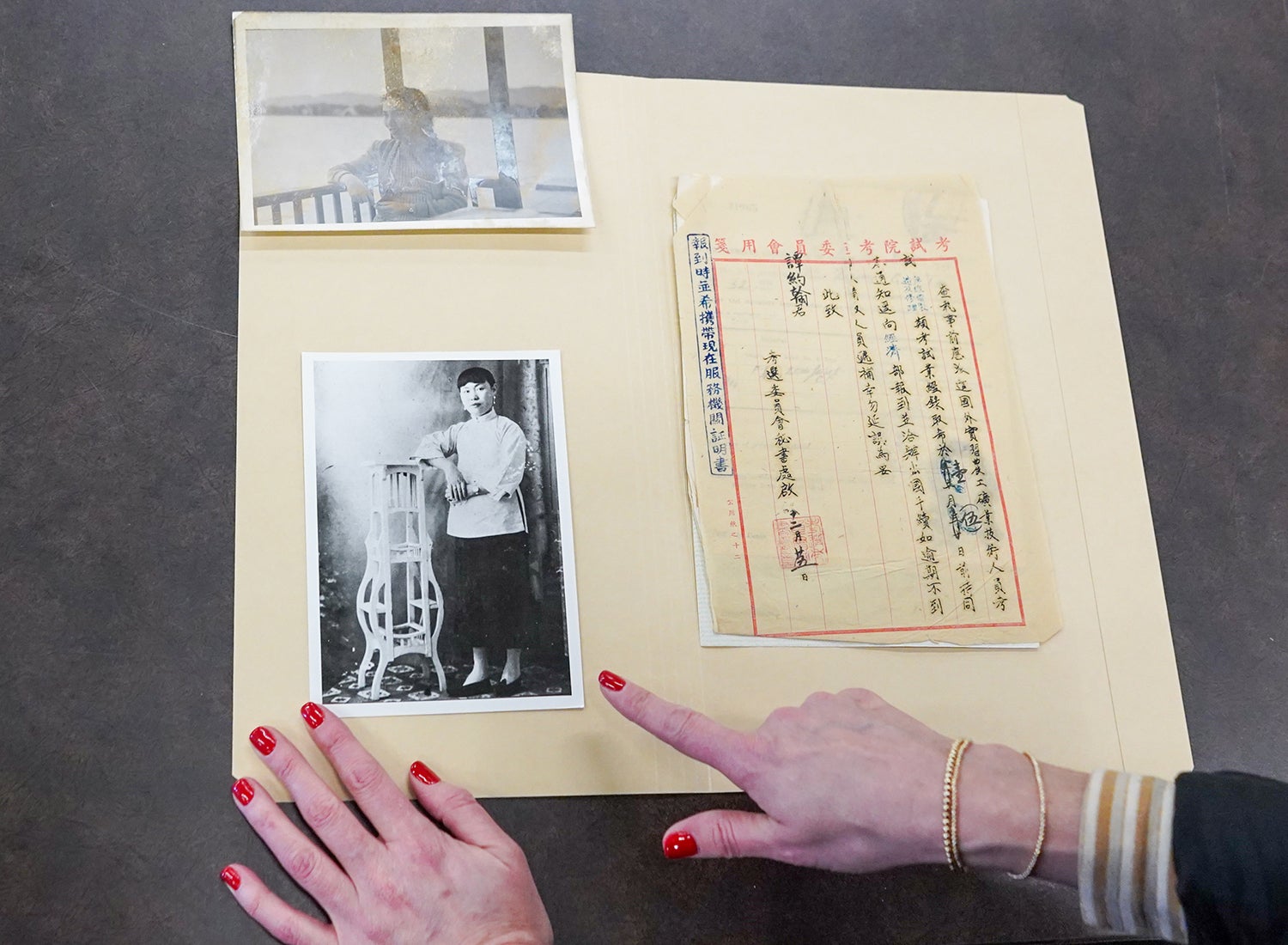 Two hands pointing to an old black and white photo of a Chinese woman next to a document handwritten in Chinese