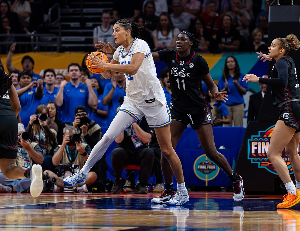 A UCLA woman basketball player holds the ball while being guarded by two other players from South Carolina