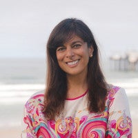 Headshot of a woman with shoulder-length hair standing in front of the ocean and a pier in the background