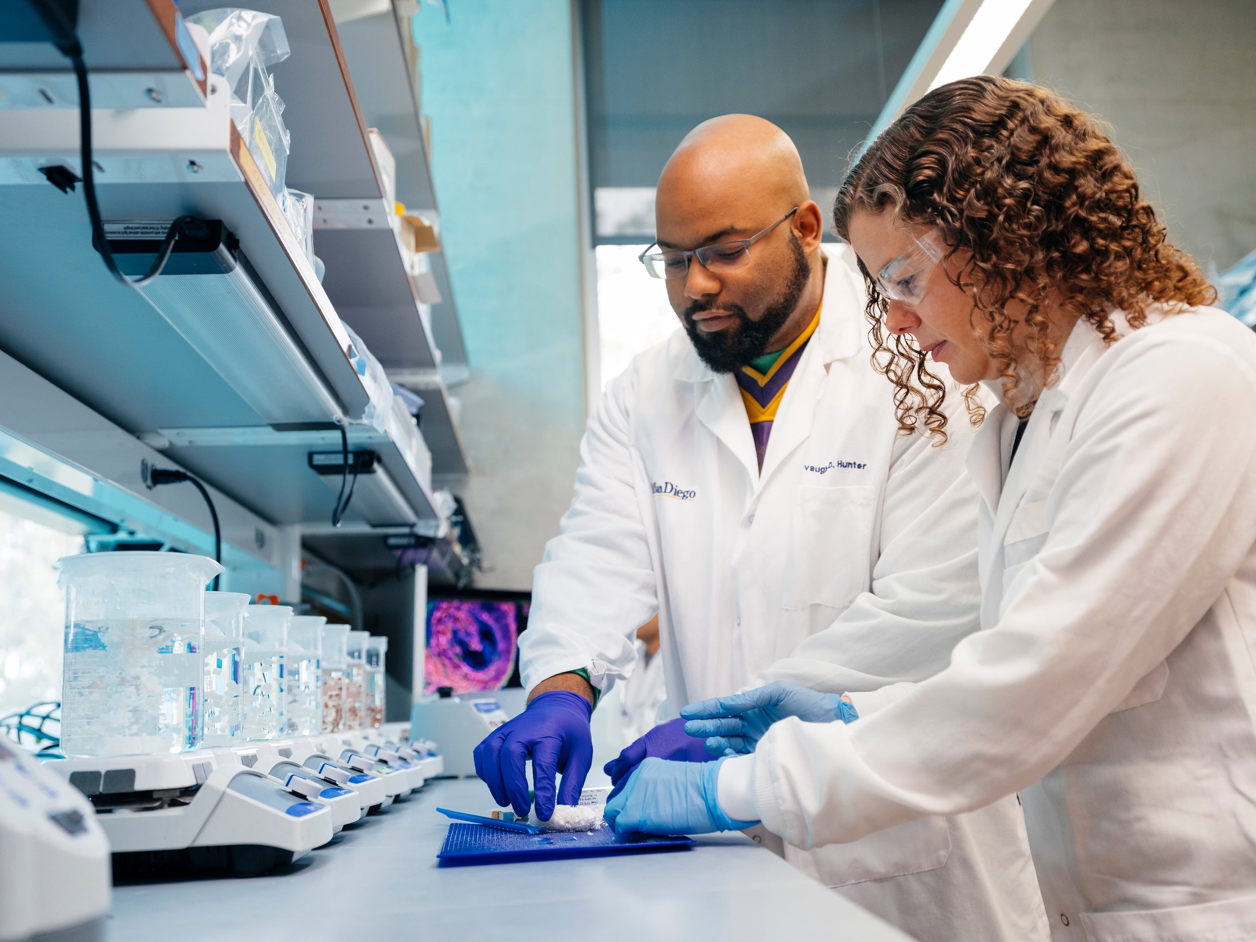 Two scientists in white lab coats work together in a laboratory.