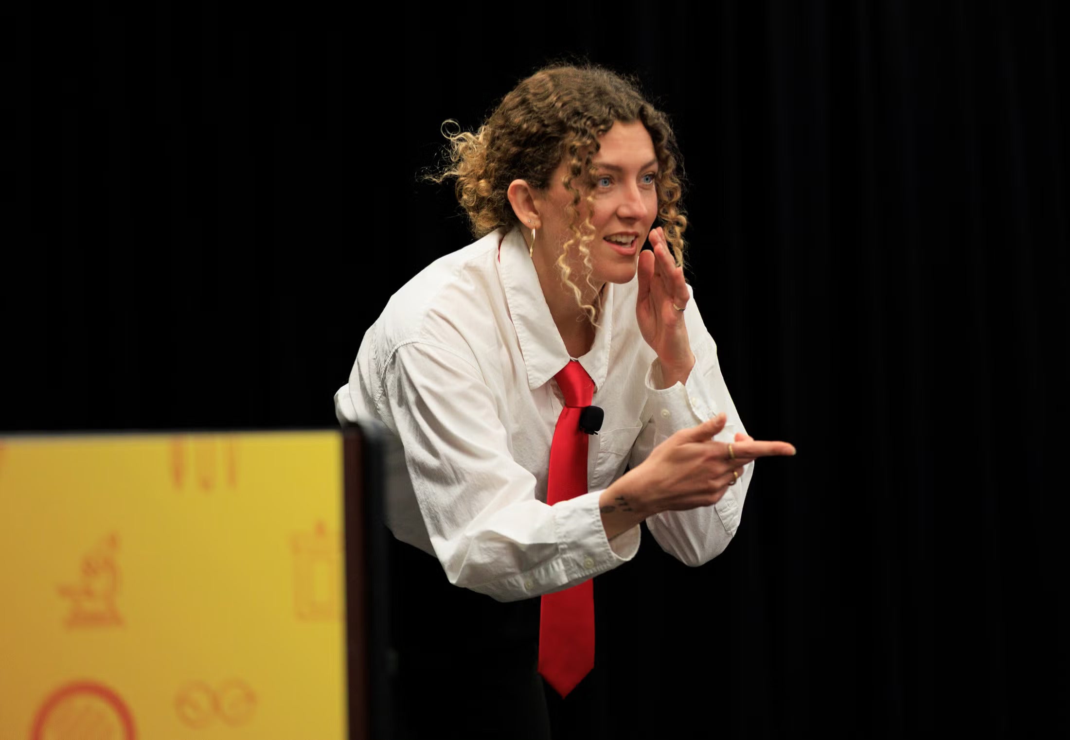A woman in a white blouse and red tie makes a chopping gesture while pointing during a presentation