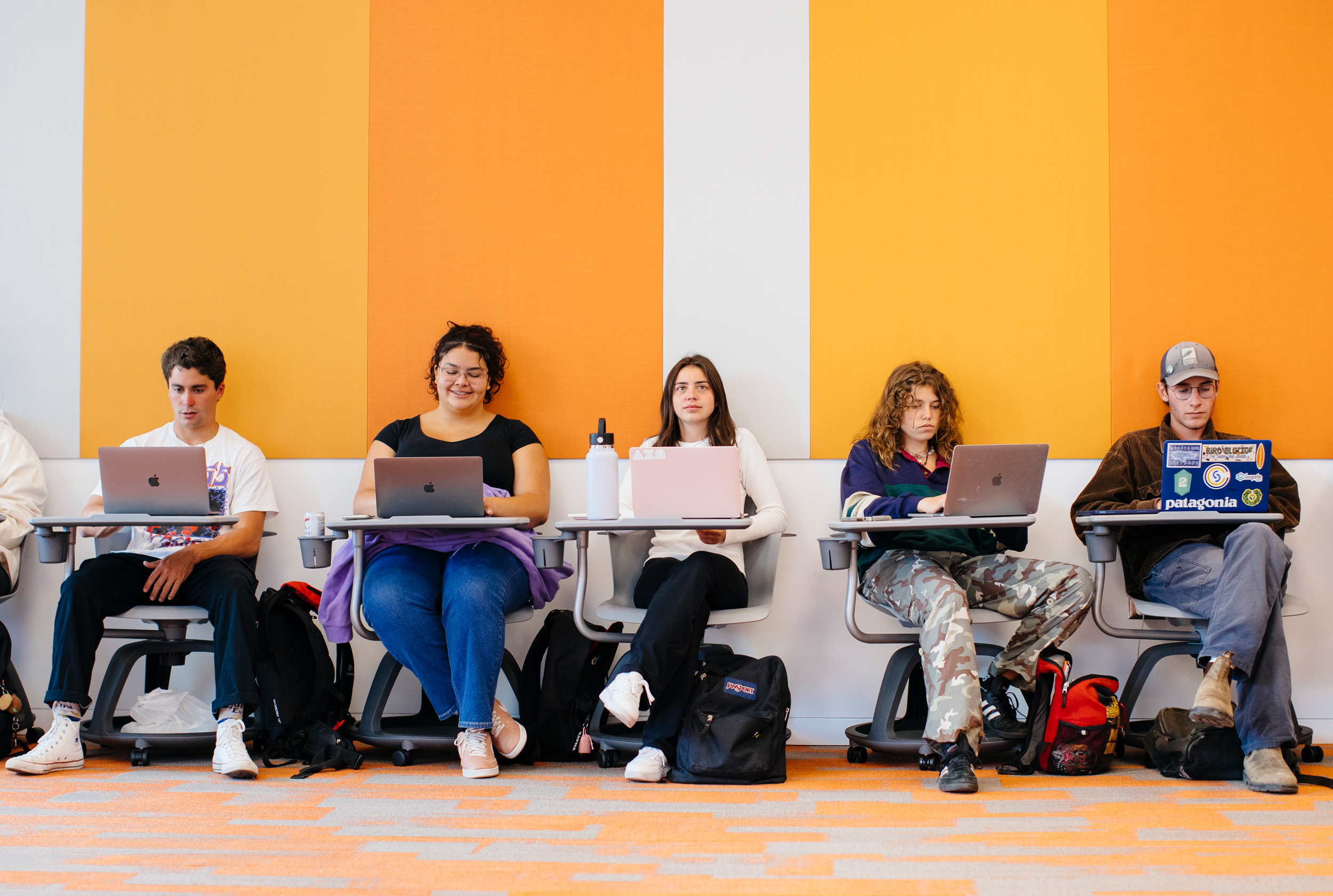 A row of students on laptops sitting at desks in a classroom