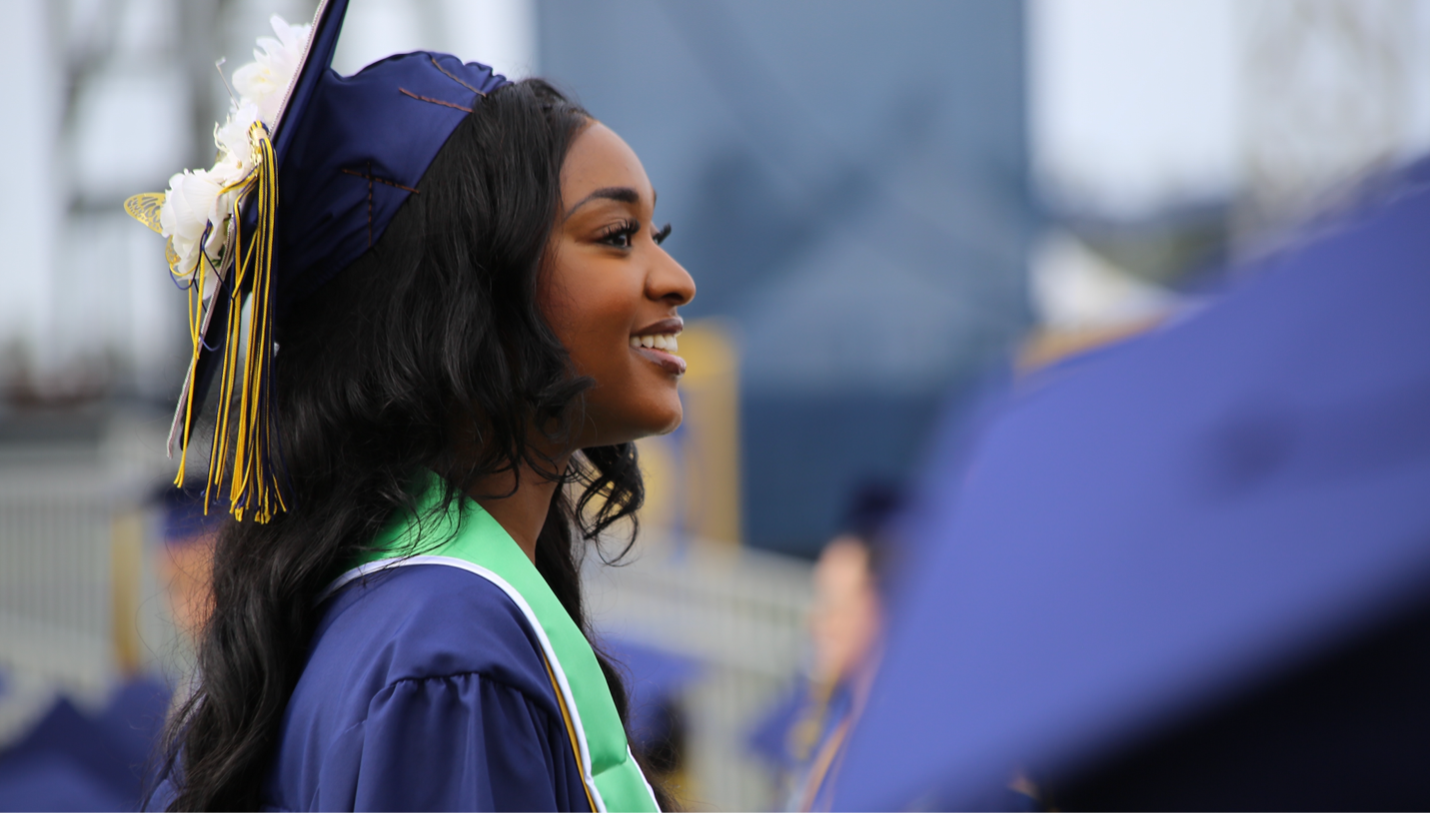 A young woman in a cap, gown and stole looks on happily during a graduation ceremony