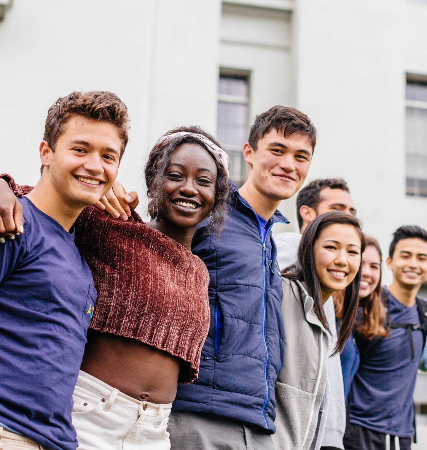 A group of smiling students stand side by side with arms wrapped around one another's shoulders