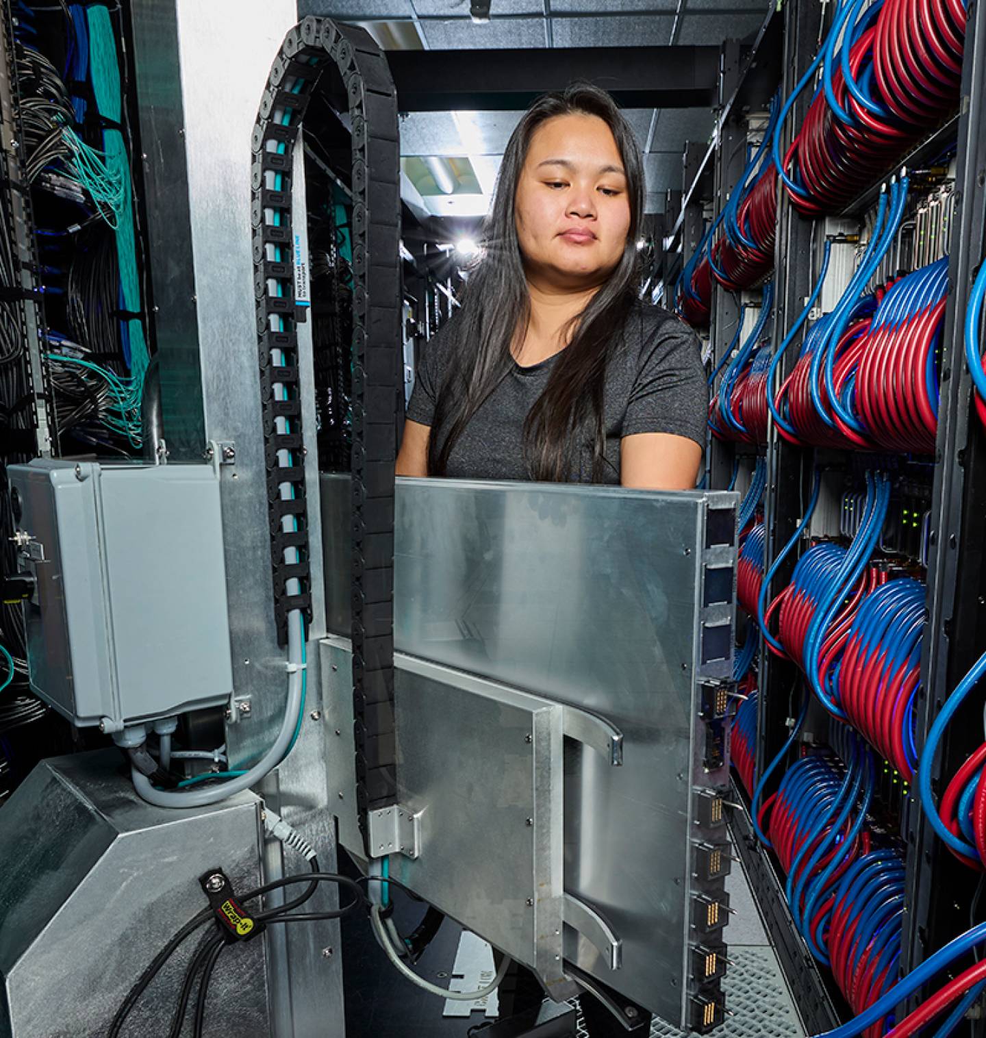 A person inside a server room filled with red, blue and green cables