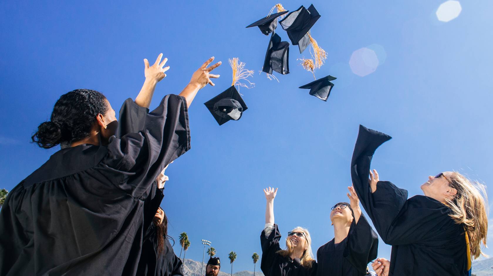 College graduates in black robes throwing their caps in the air against a blue sky