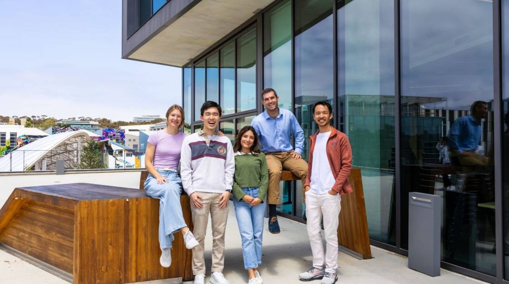 Five young people smile for the camera on an outdoor patio of an academic building