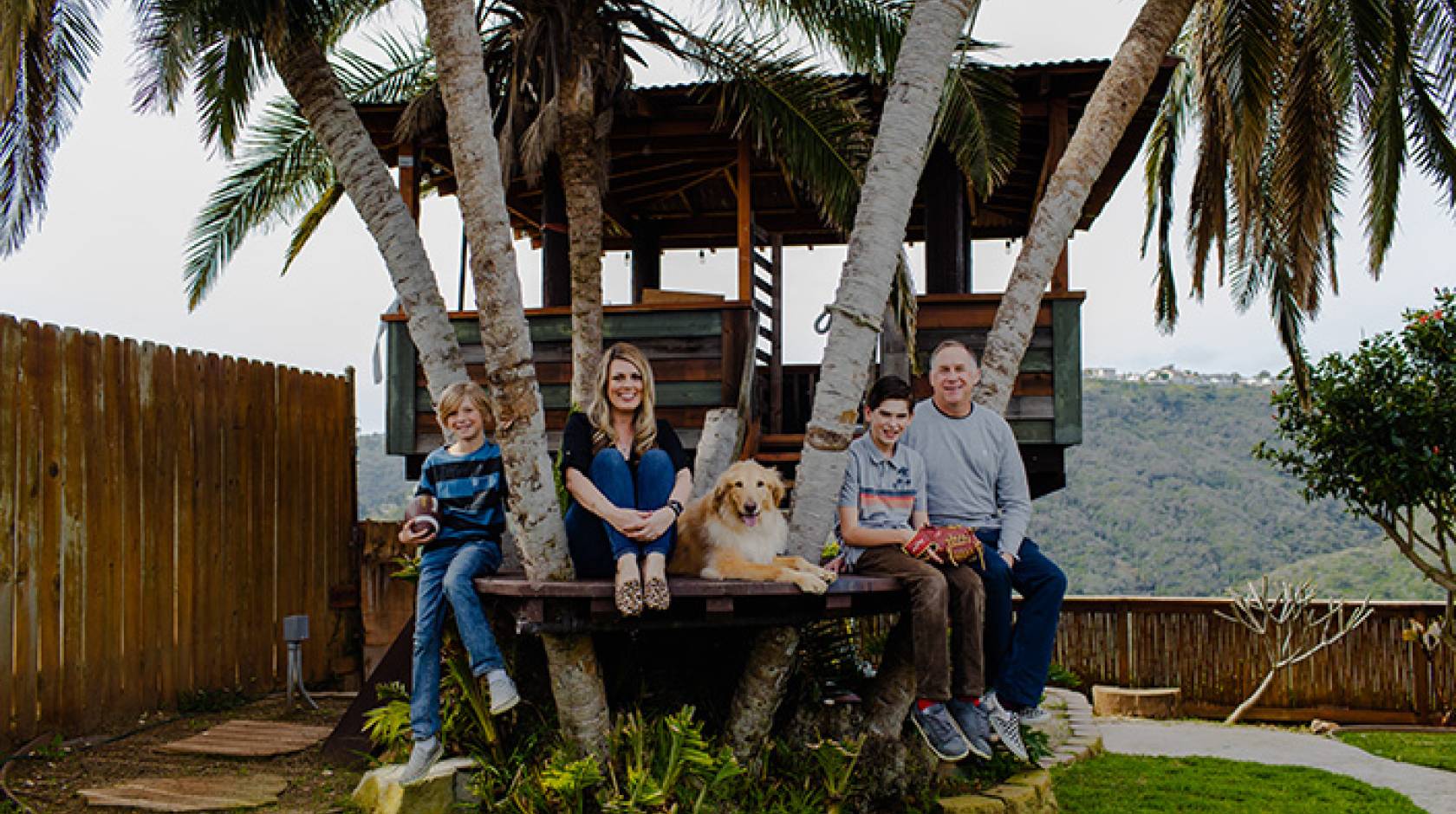 A family of four, with a golden retriever, sits together in a treehouse