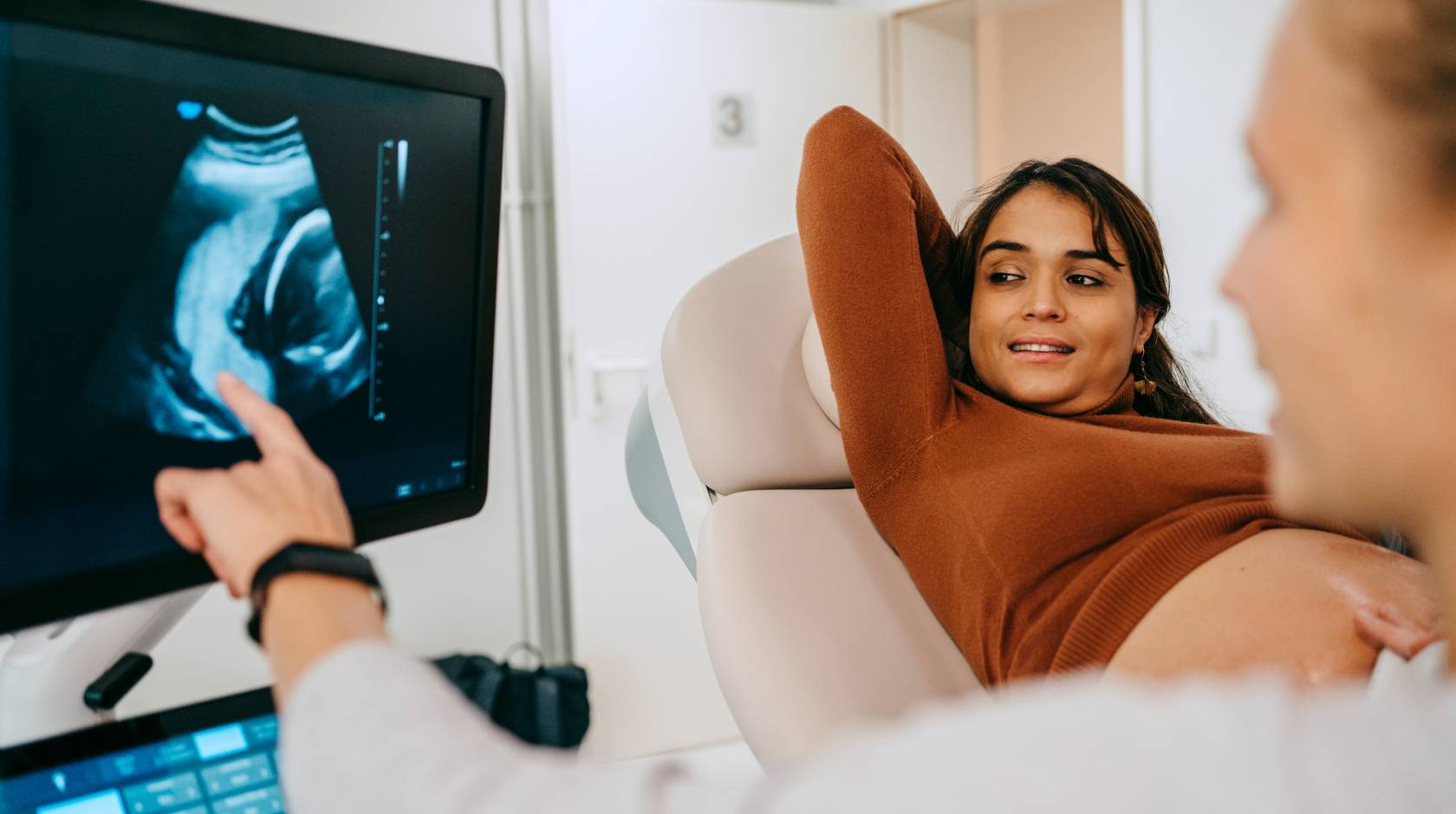 A woman looks happily at an image of her fetus on a screen as a nurse points