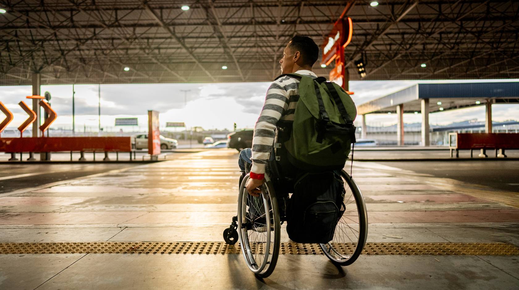 A person in a wheelchair with a backpack on is about to cross a roadway at a crosswalk