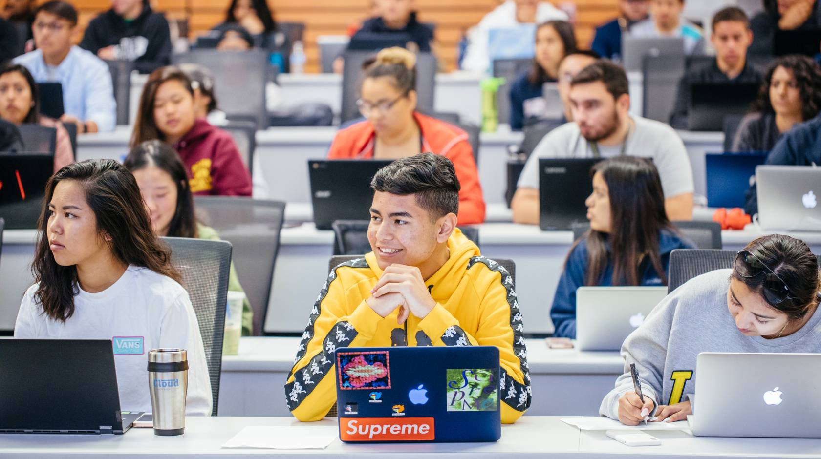 students sitting in a lecture hall listening and engaged, each with an open laptop
