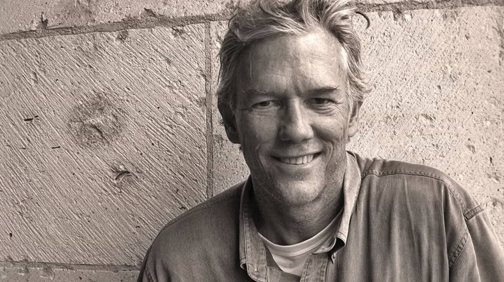 William Finnegan smiles against a brick wall in a sepia-tinted image