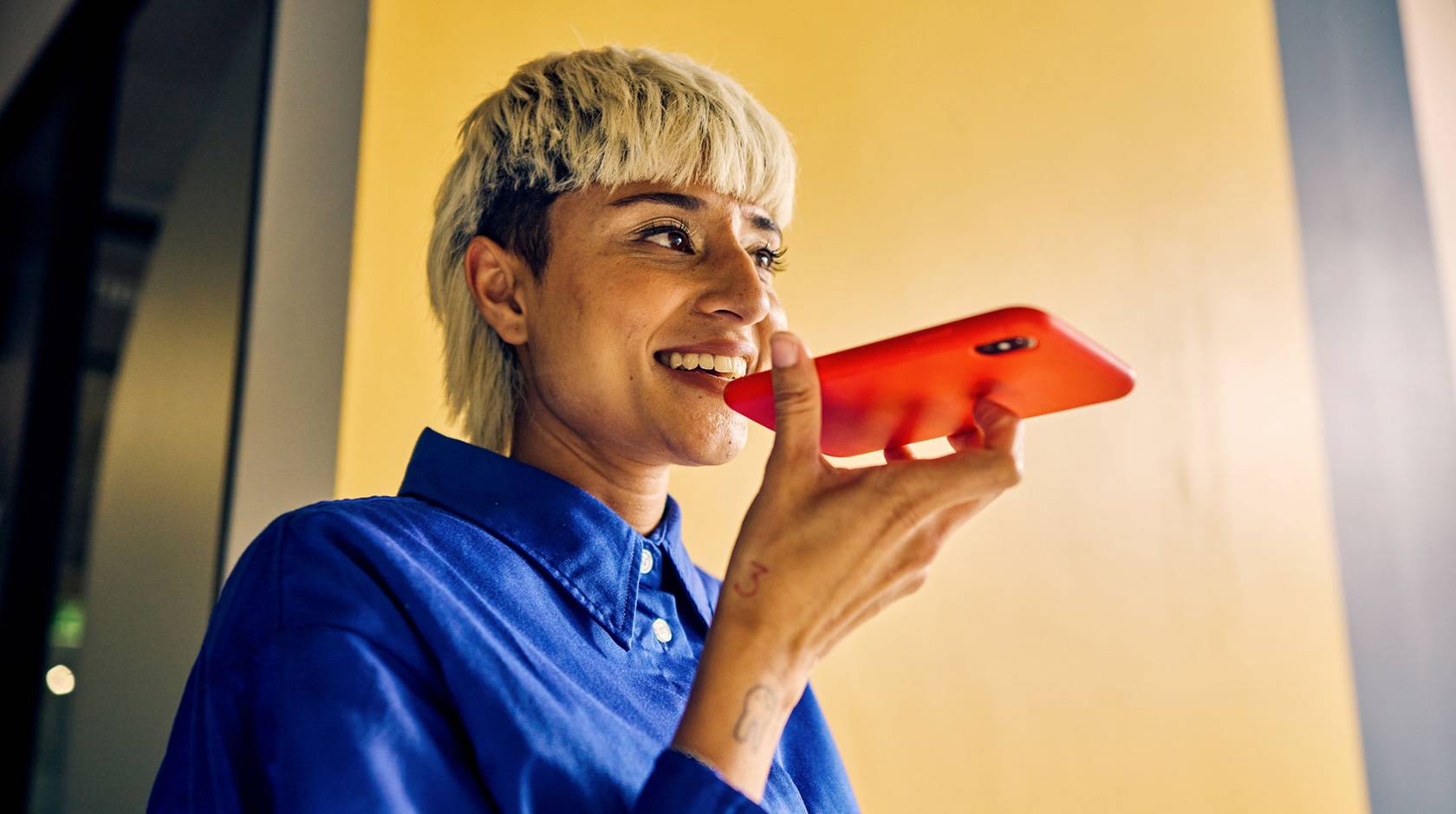 A young woman with a distinctive haircut speaks into a smart phone, smiling