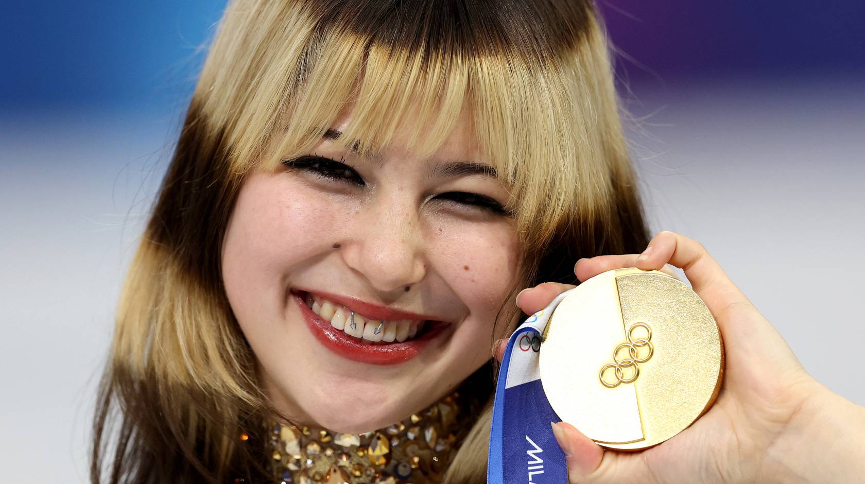 A woman holds up a gold medal and smiles