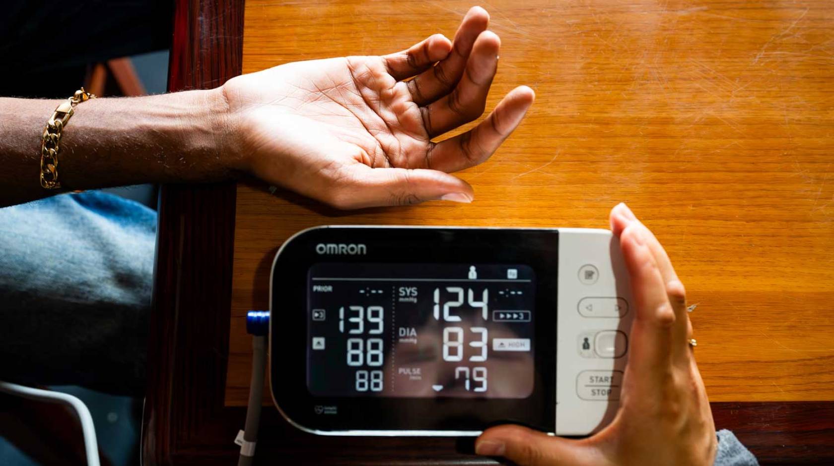 A hand is extended while another hand holds a blood pressure monitor with readings on it