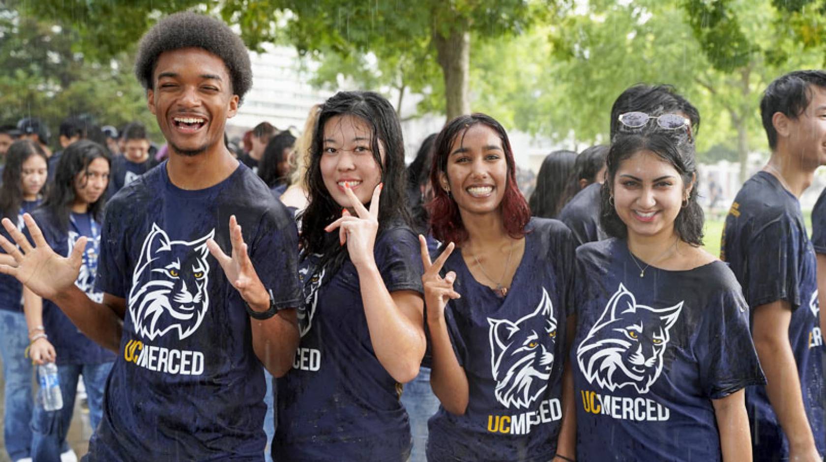 Five students wearing UC Merced Bobcat t-shirts smile for the camera in a downpour