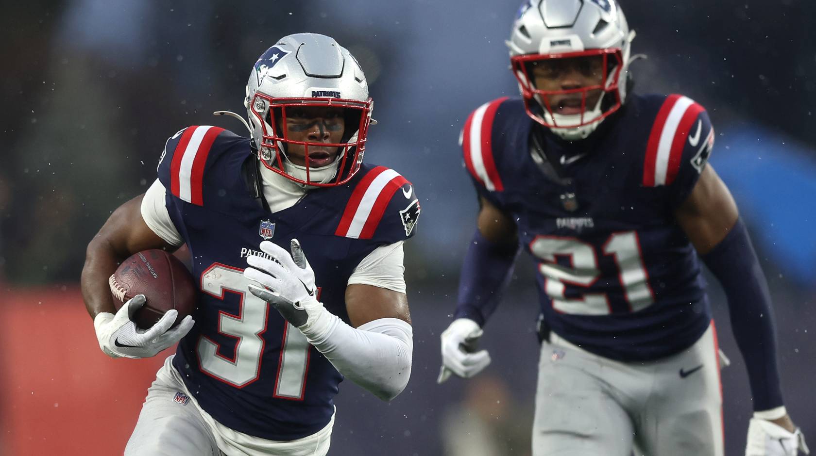 Two players for the New England Patriots, one holding the football and running
