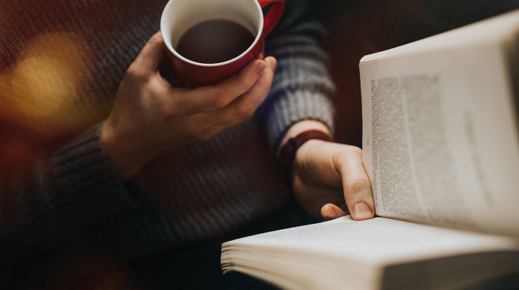 A view of someone holding a cup of coffee and reading a book from above