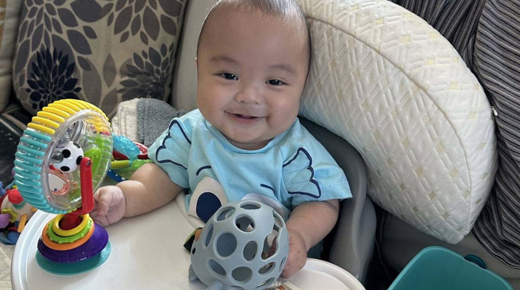 A baby smiles at the camera and plays with toys in a bouncy seat