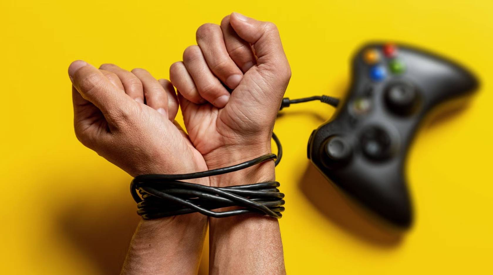 A pair of hands with wrists bound by a gaming console cord