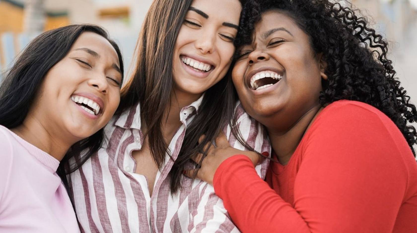 Three women laugh while in a group hug