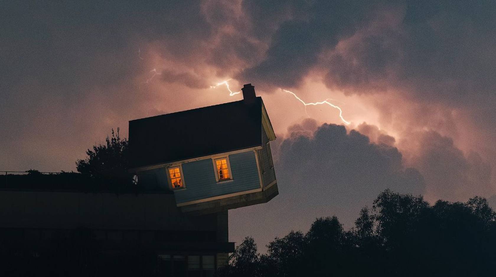 The leaning/falling house installation on the UC San Diego campus with a lightning sky backdrop