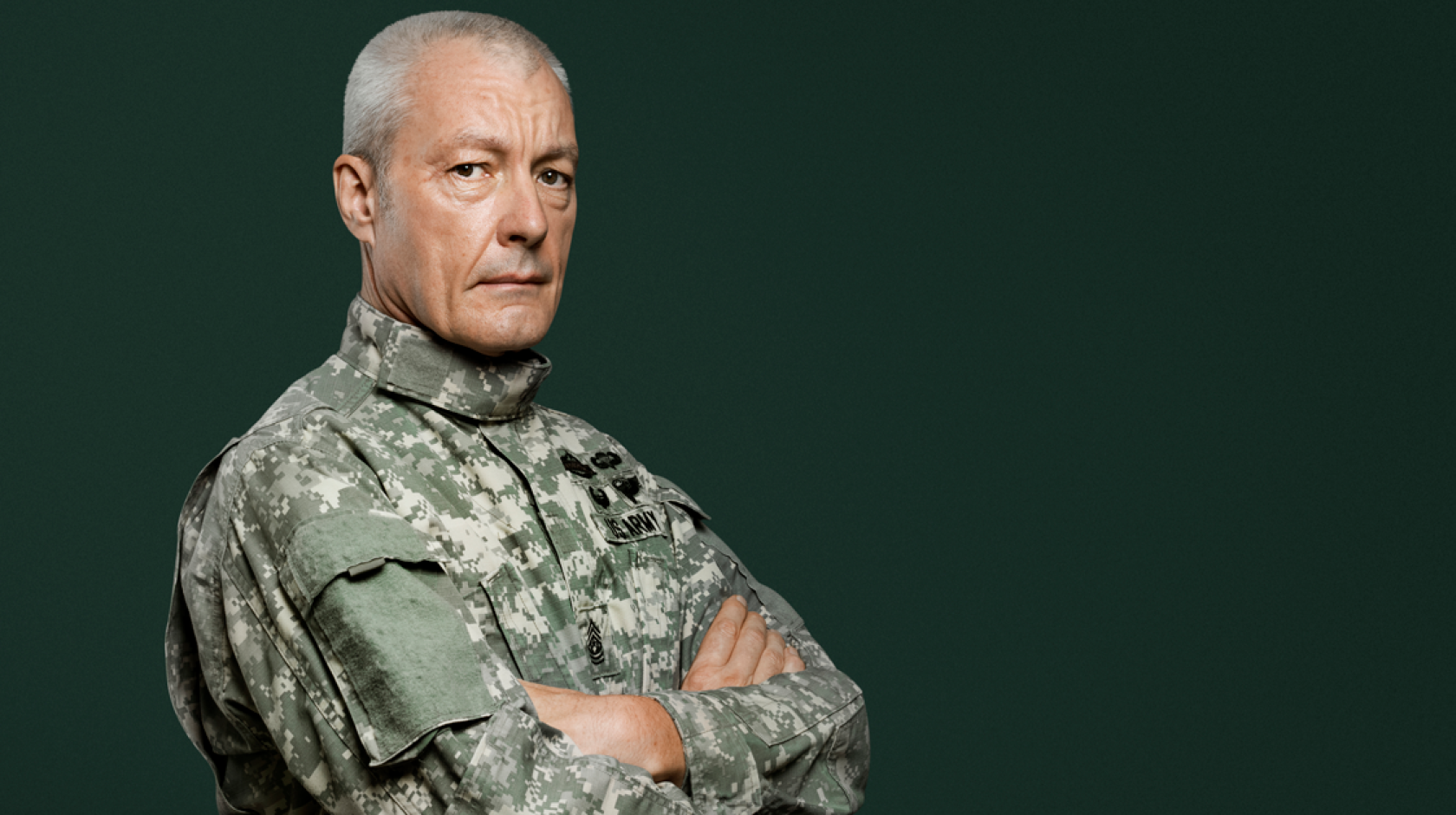 A man in military uniform stands with his arms folded across his chest.