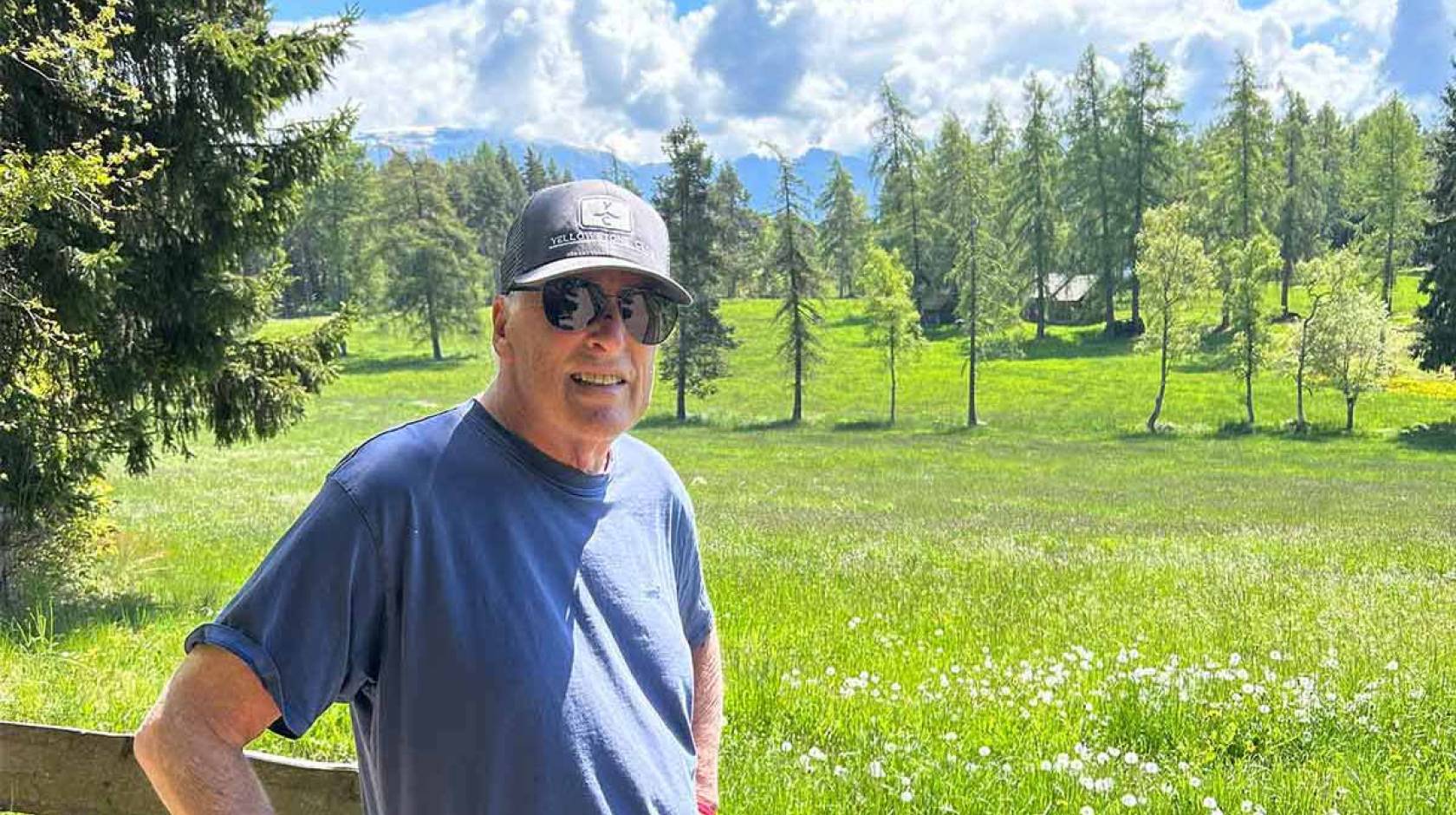 A man wearing a ballcap stands in the Sierras on a beautiful day
