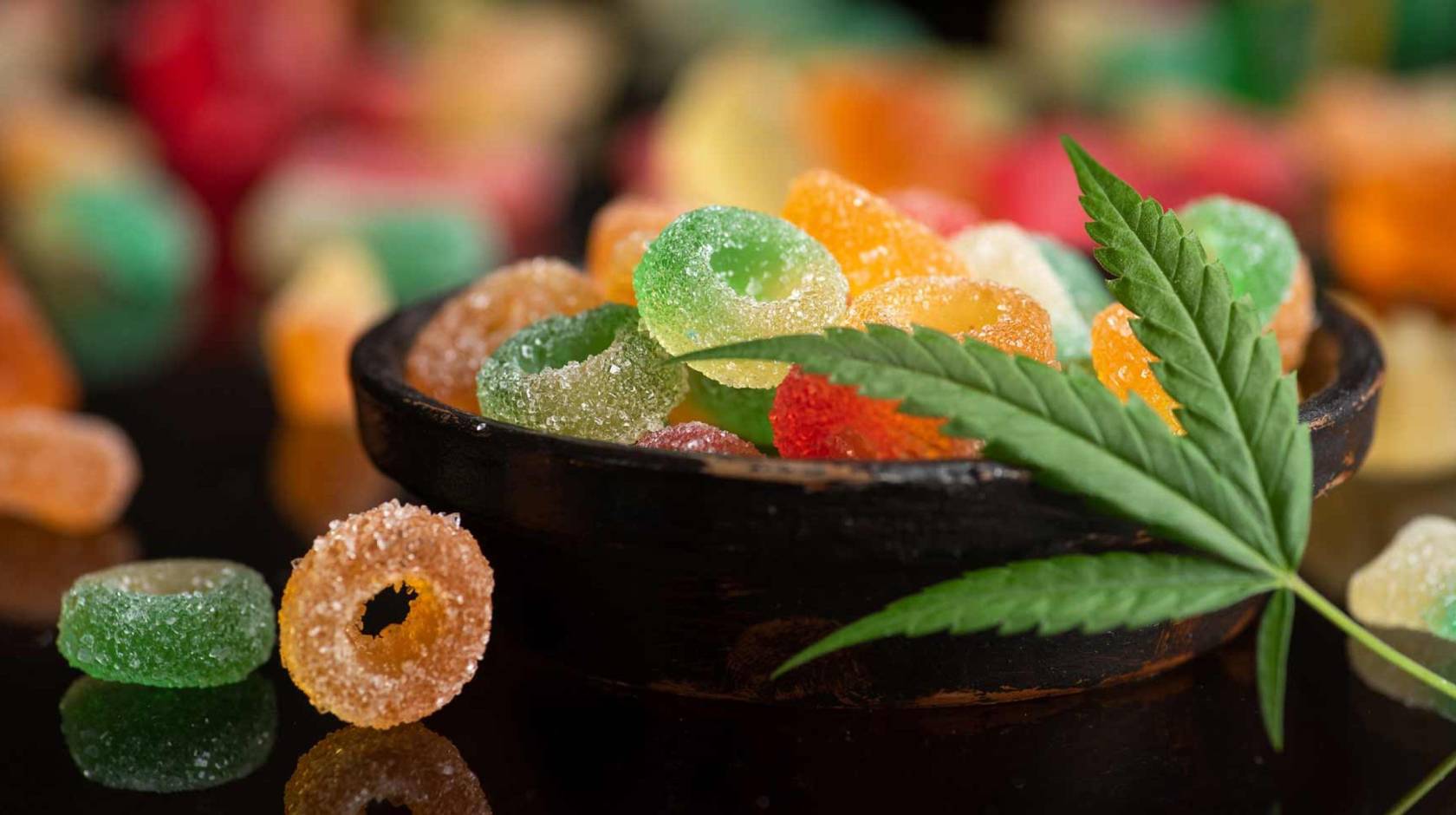 A bowl of gummies with a marijuana leaf draped over it