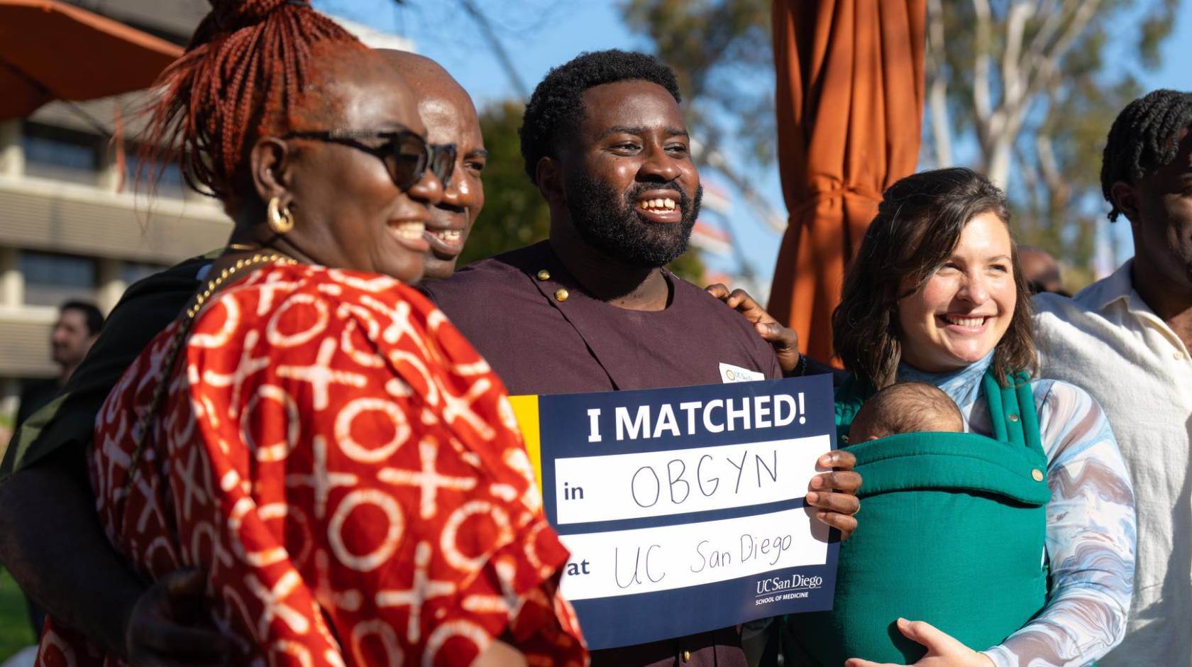 A family with a newborn smiles holding a sign that says I Matched! OB/GYN at UC San Diego at the campus' Match Day