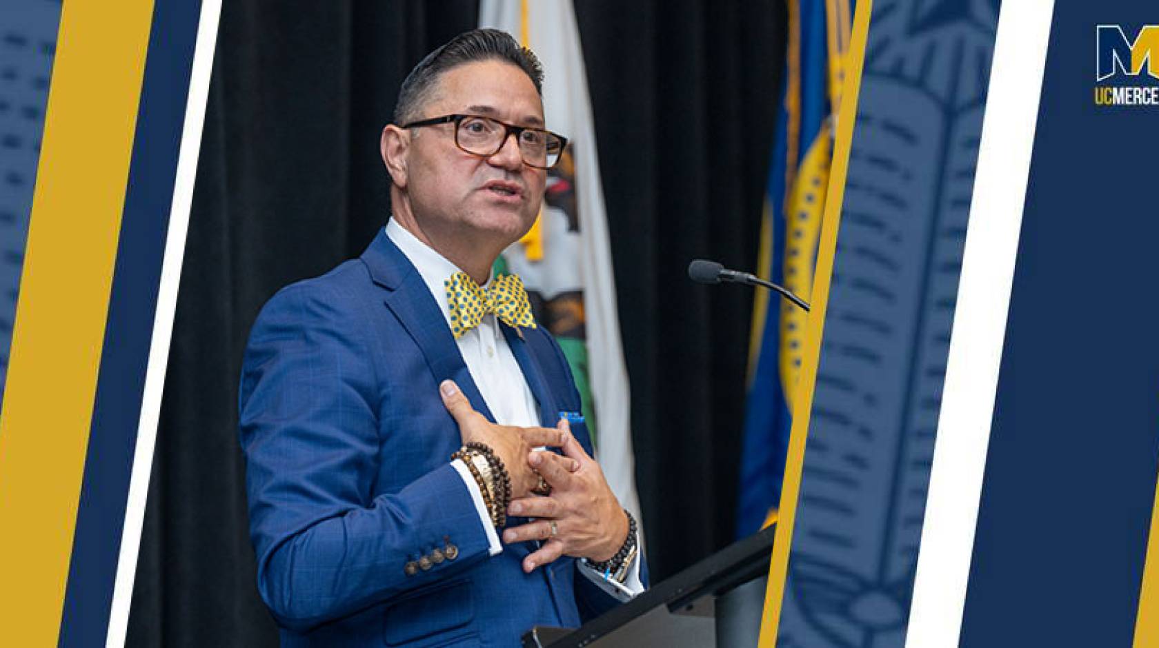 Juan Sánchez Muñoz in a blue suit speaks at a podium, holding both hands to his chest