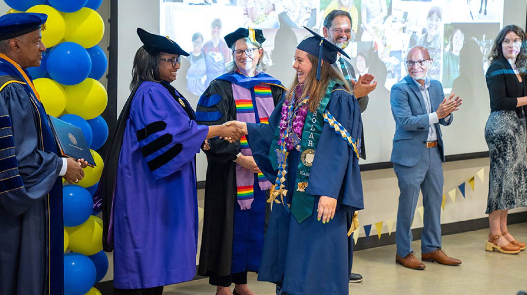 A UC Davis graduate in graduation robe and cap receiving her diploma from university leaders dressed in academic regalia