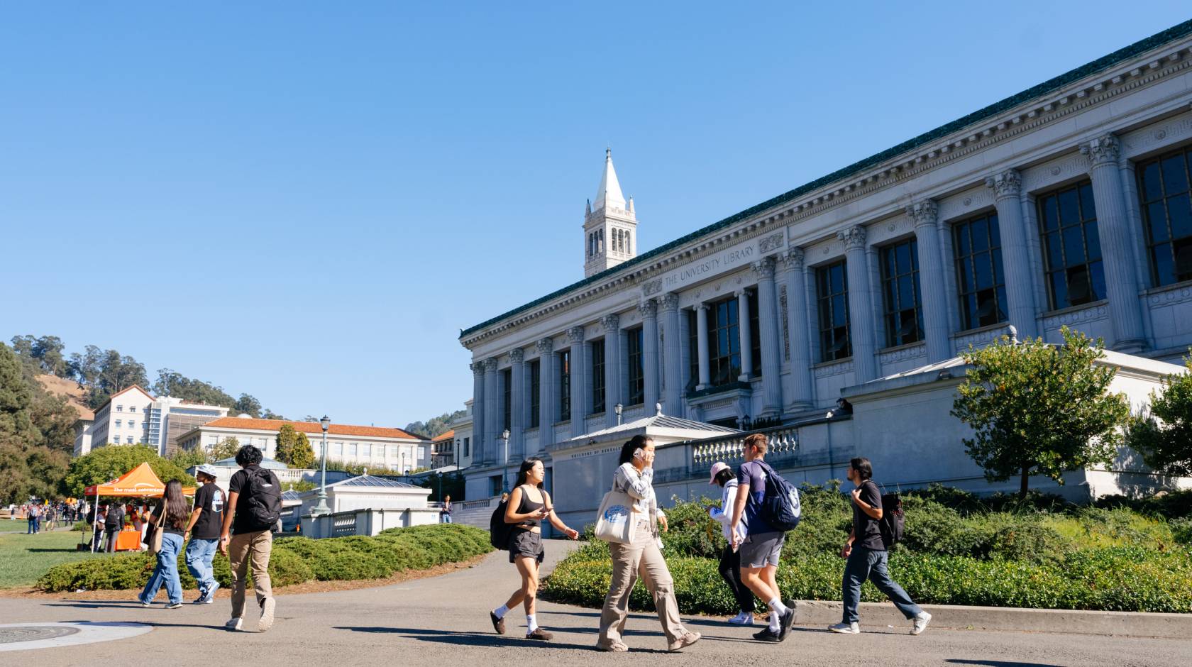 Students walk on the UC Berkeley campus, Campanile behind them