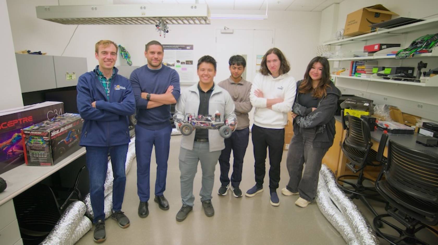 6 people stand in a lab, one holding a small robotic car