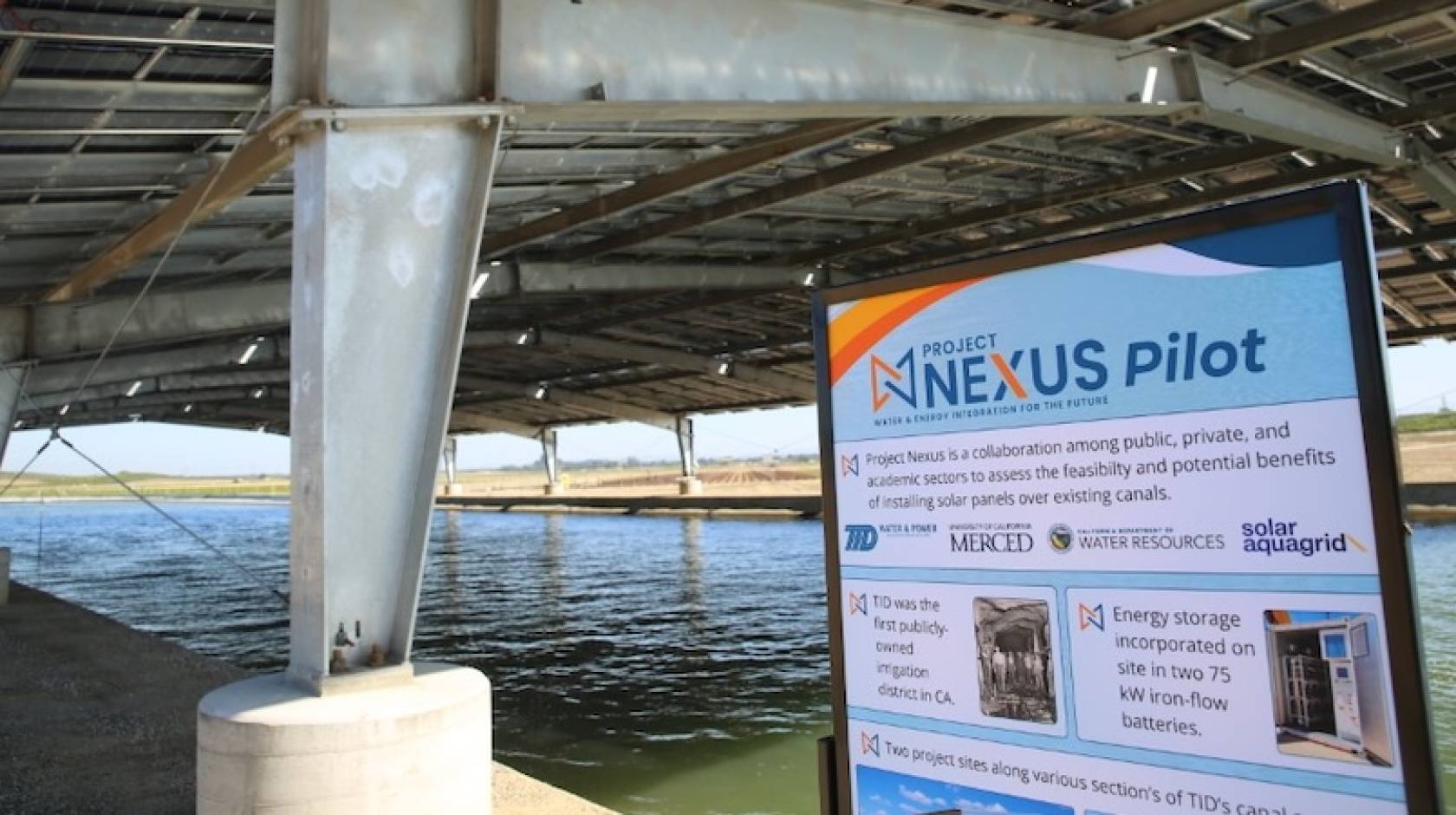 A water canal covered by a solar panel canopy, with a sign for the Nexus project pilot