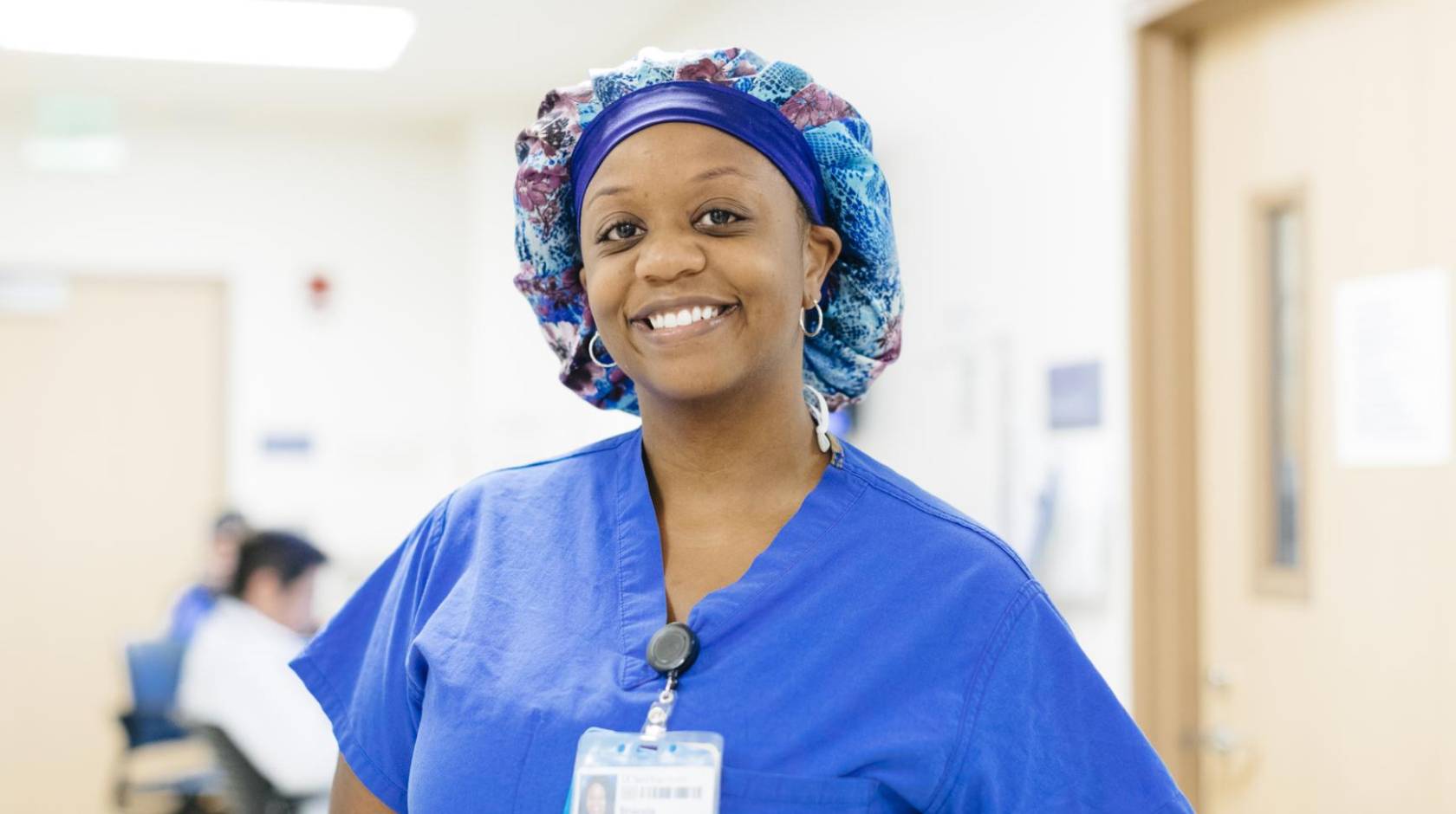A nurse in scrubs and a hairnet smiles