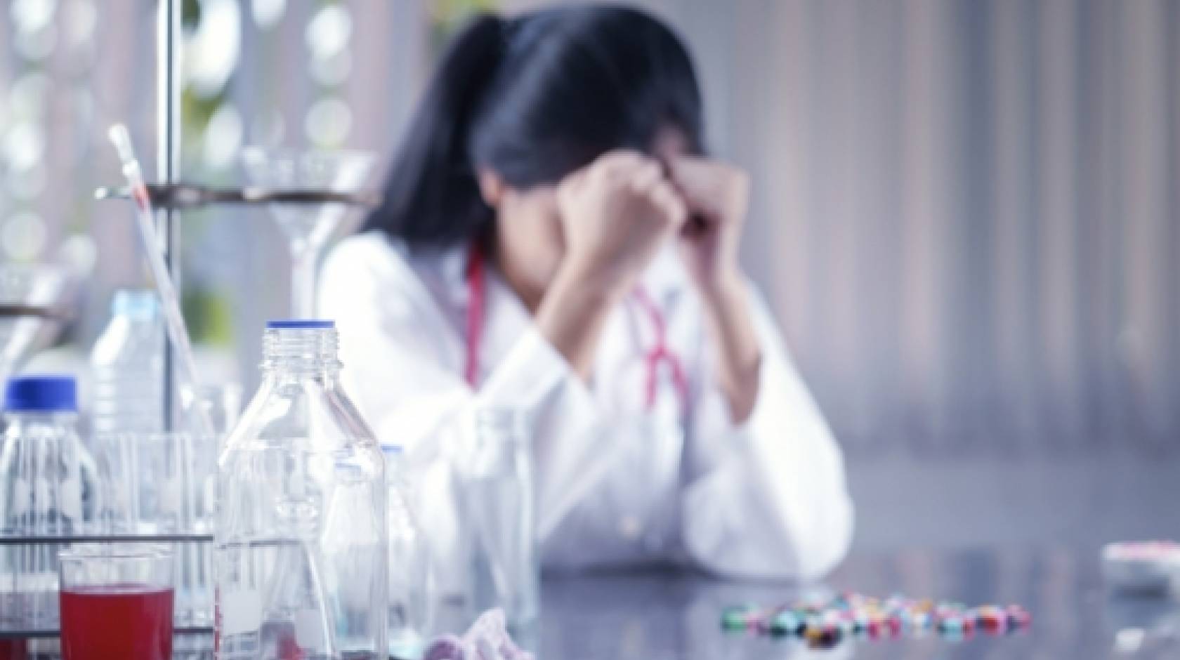 Woman in a lab coat, hangs her head down.