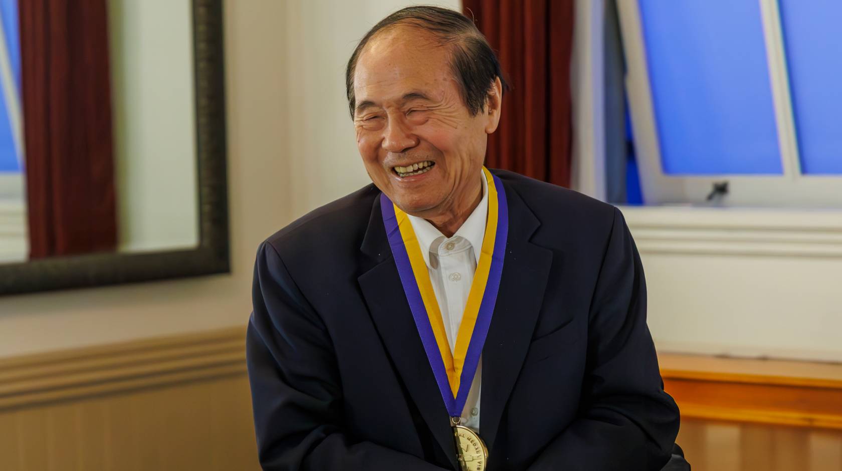 Chancellor Henry T. Yang smiles widely with his hands clasped as he wears his UC Presidential medal