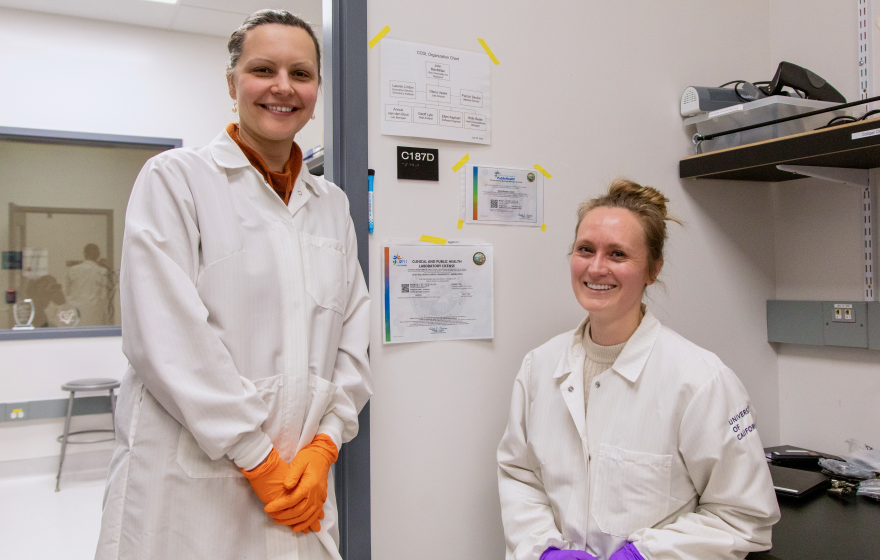 Two researchers wearing lab coats and brightly colored gloves