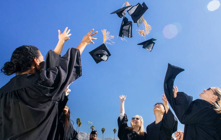 College graduates in black robes throwing their caps in the air against a blue sky