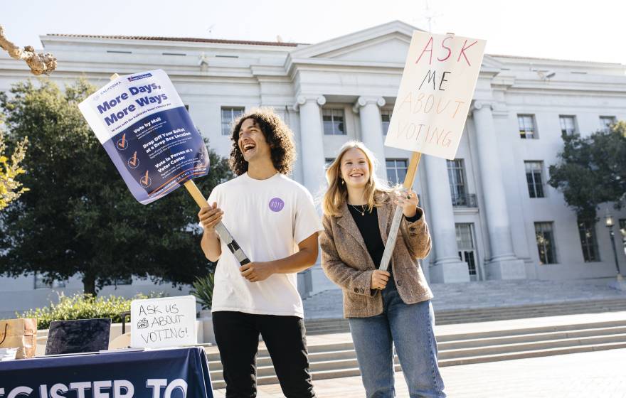 Students Alex Edgar and Skylar Betts hold signs about voting on Sproul Plaza