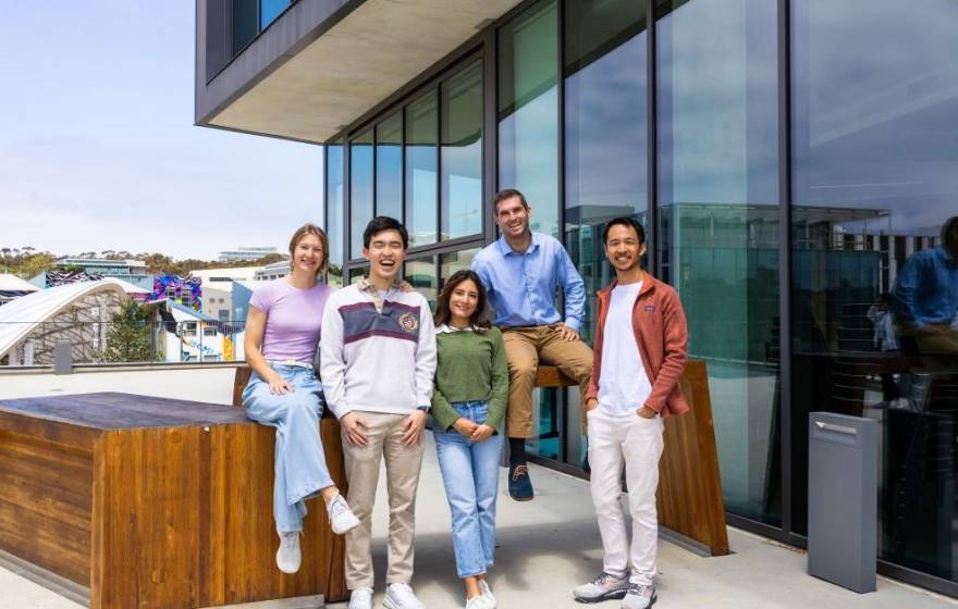 Five young people smile for the camera on an outdoor patio of an academic building