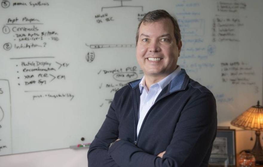 John Chaput, UCI professor of pharmaceutical sciences, stands smiling in front of a white board that is covered with notes.