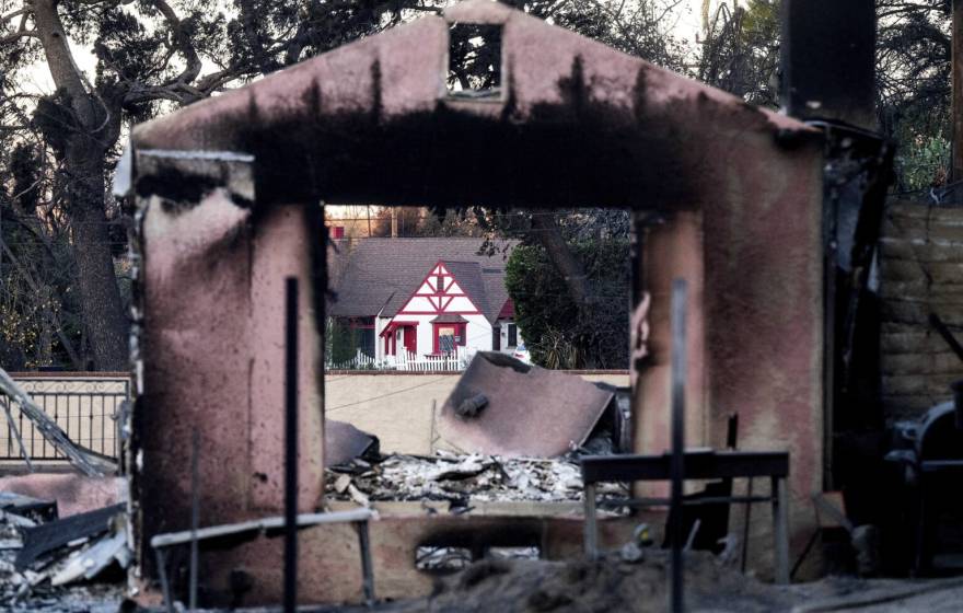 A home destroyed by the Eaton Fire stands in front of a home that survived in Altadena.