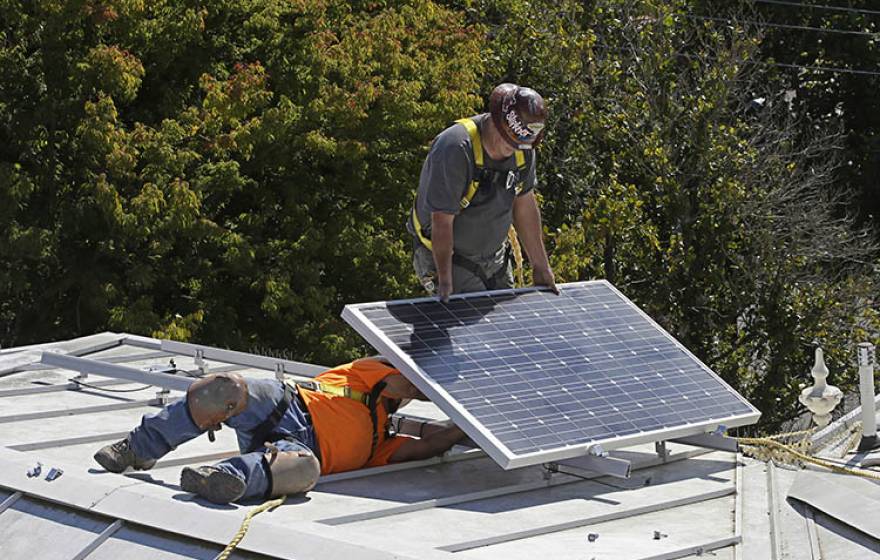 Workers install solar panels on a roof