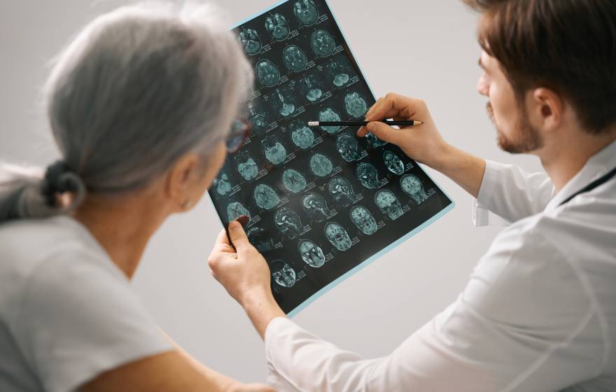 Doctor diagnostician holds an MRI scan of the brain in his hands, he consults an elderly lady