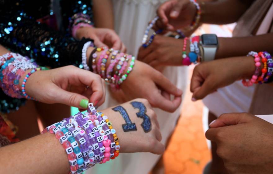 Closeup of the hands of a group of Taylor Swift fans wearing stacks of colorful friendship bracelets