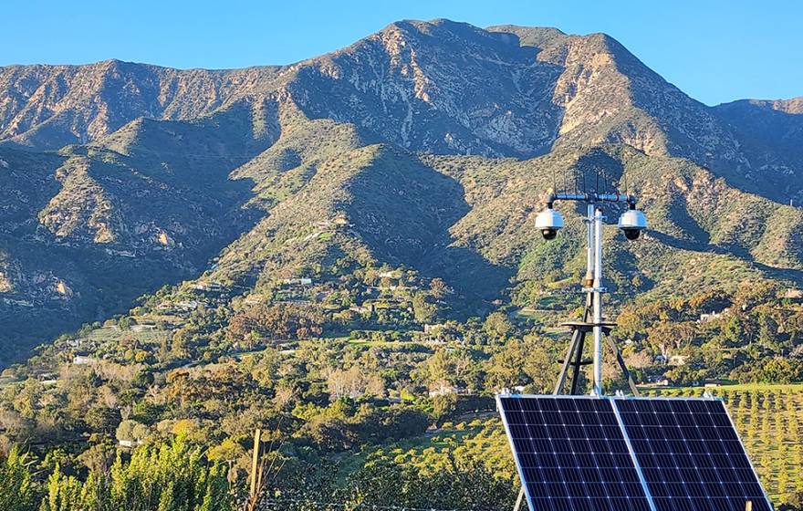 A solar panel and a camera with the mountains of Ortega Ridge behind